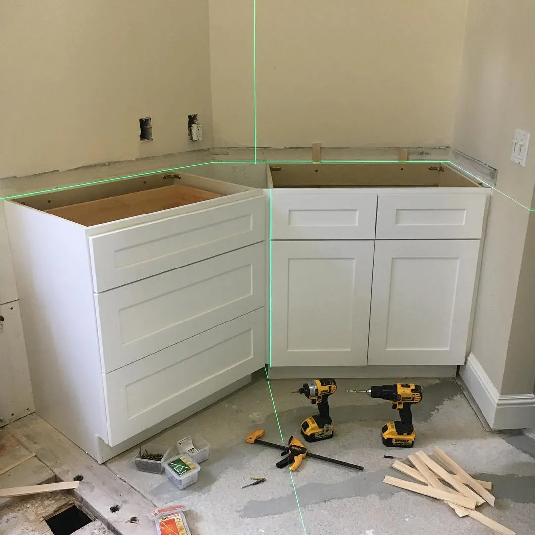 White shaker base cabinets with drawers being installed in a Santa Rosa bathroom corner using a laser alignment tool