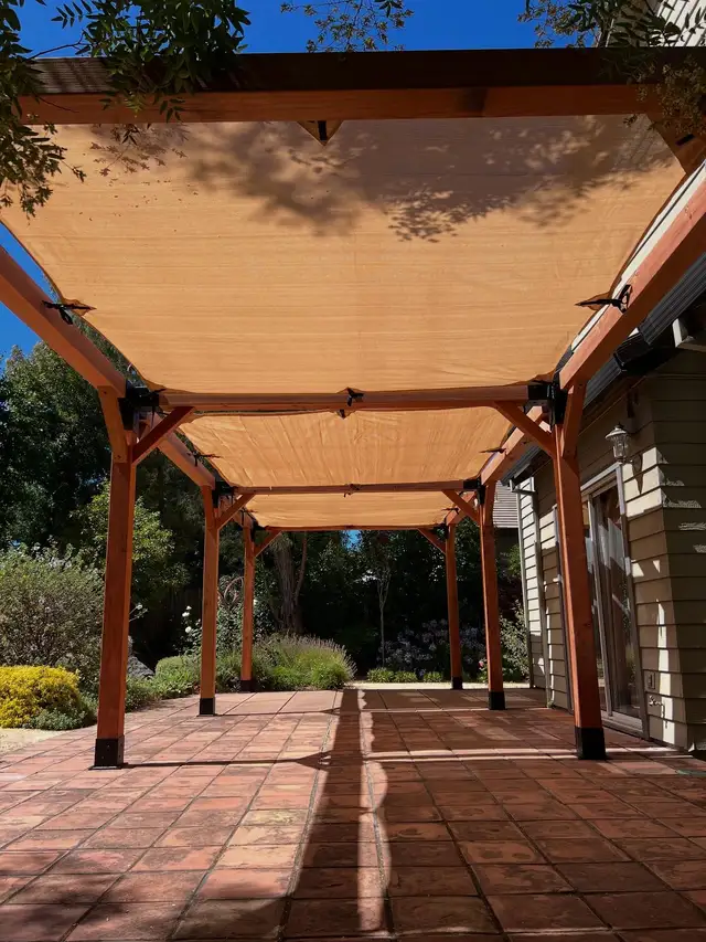 Redwood pergola with retractable fabric shade canopy over a paver patio attached to a house in Sonoma
